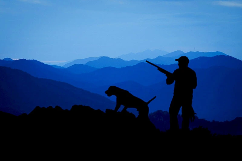 photo of a hunter and his dog at twilight